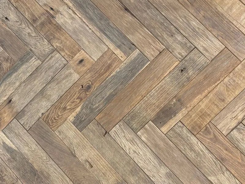 Detailaufnahme eines Fischgrätparketts aus alter Eiche mit charaktervoller Holzmaserung und warmen Brauntönen.